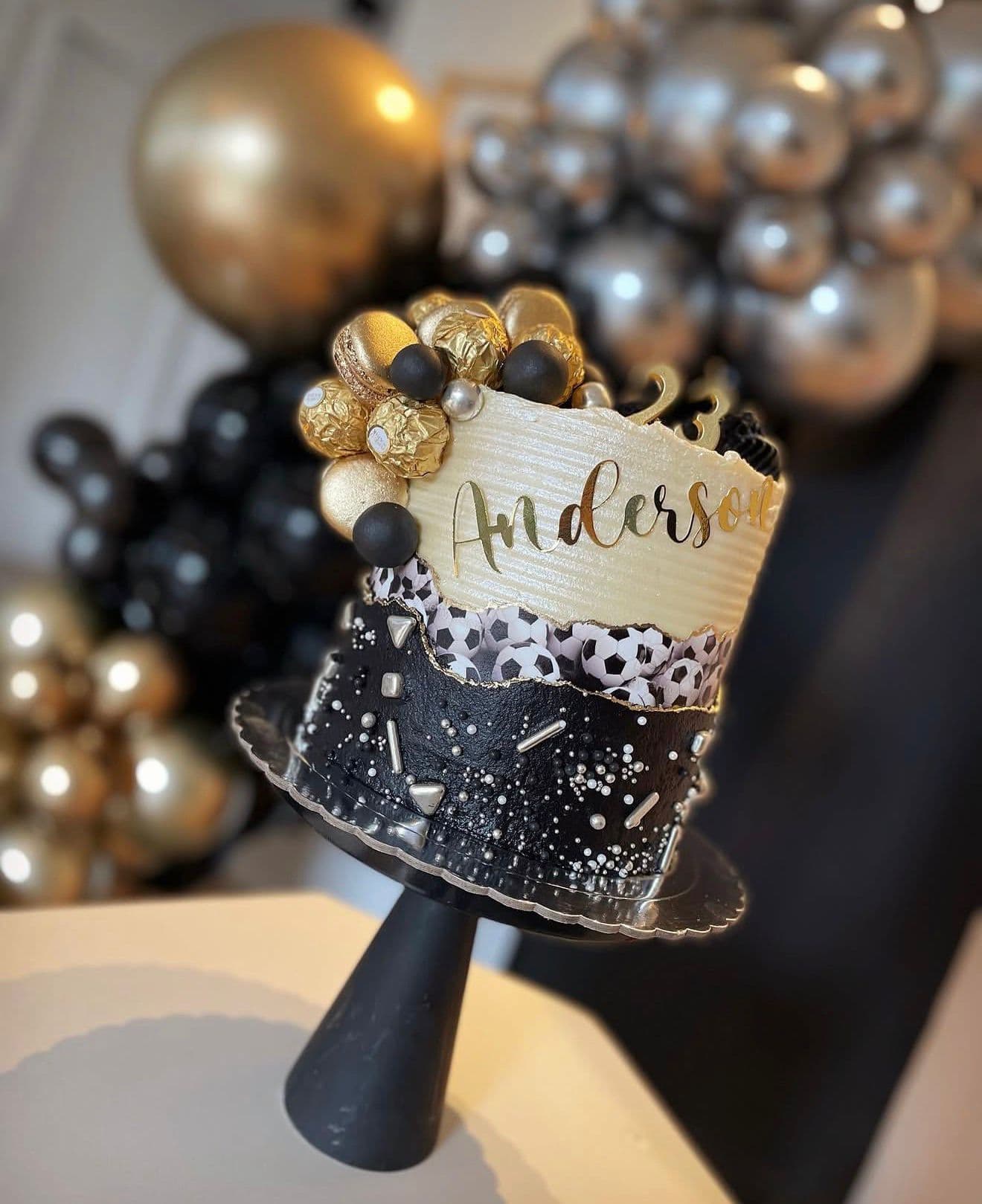 Tarta negra y dorada con chistera decorativa y globos